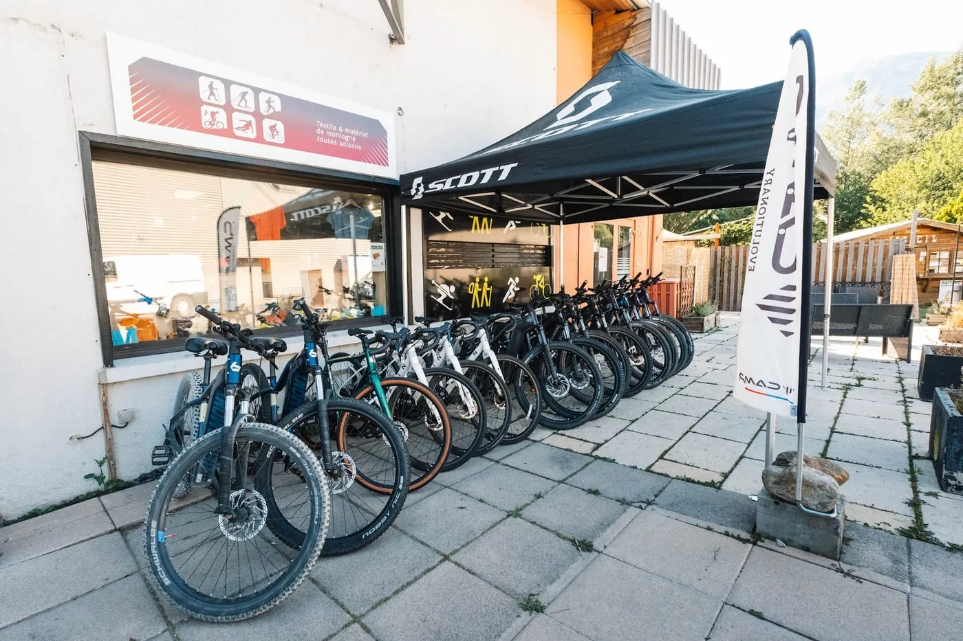 Magasin Prieur-Blanc Sports à Embrun — VTT électriques et gravels alignés devant la vitrine, sous une tonnelle